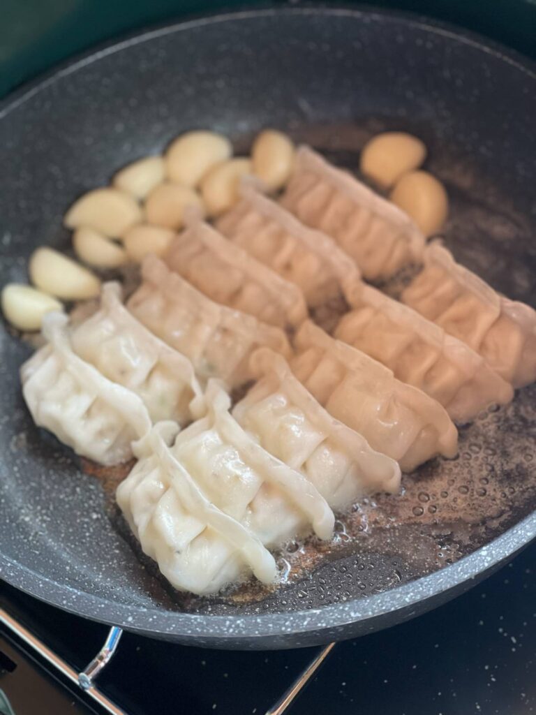 フライパンで焼かれる餃子とにんにく、外調理の様子