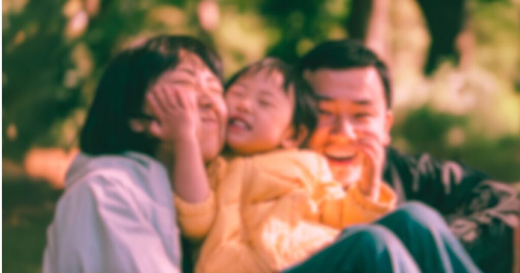 キャンプ場で笑い合う家族の様子。親子3人が寄り添い、笑顔を見せる幸せな瞬間。