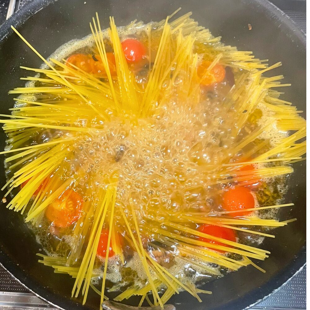 フライパンの煮汁にパスタを押し込みながら加え、茹でている様子