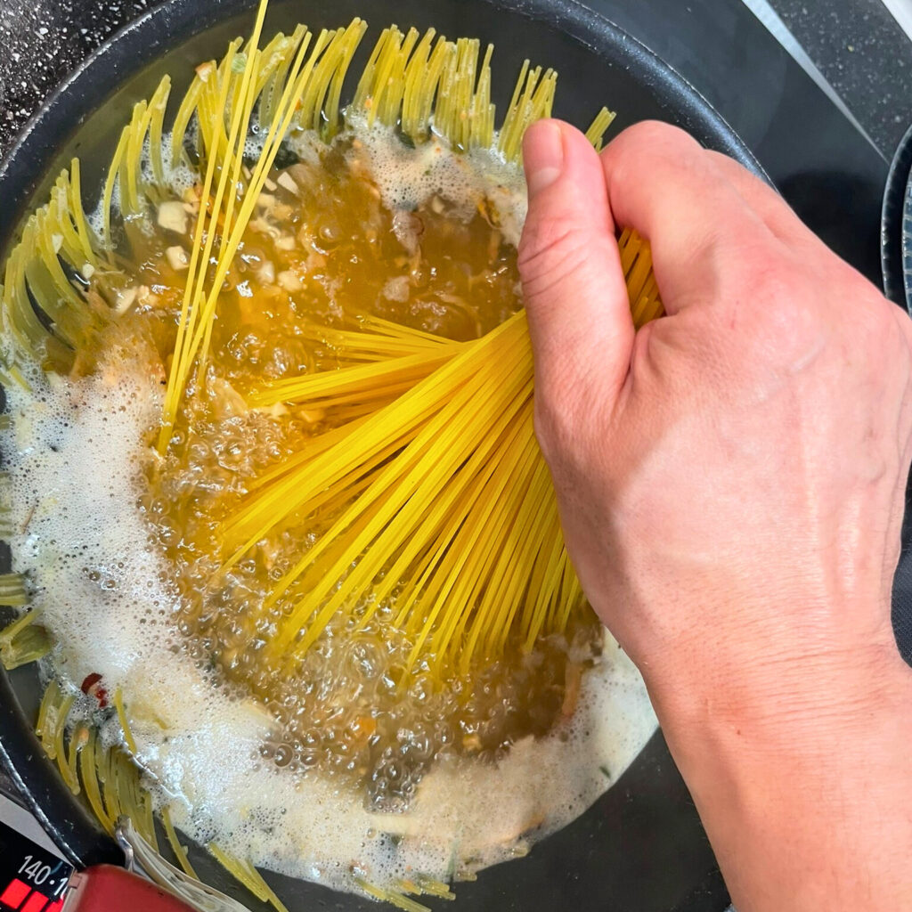 沸騰したフライパンに手でパスタを押し込んでいる様子
