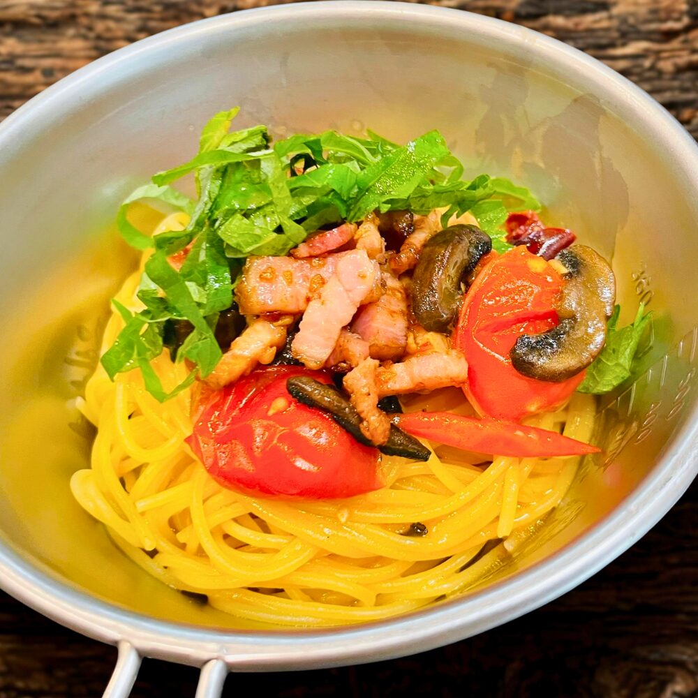 茹で上がったパスタに炒めたベーコンときのこ、トマトをのせ、大葉を散らした完成図