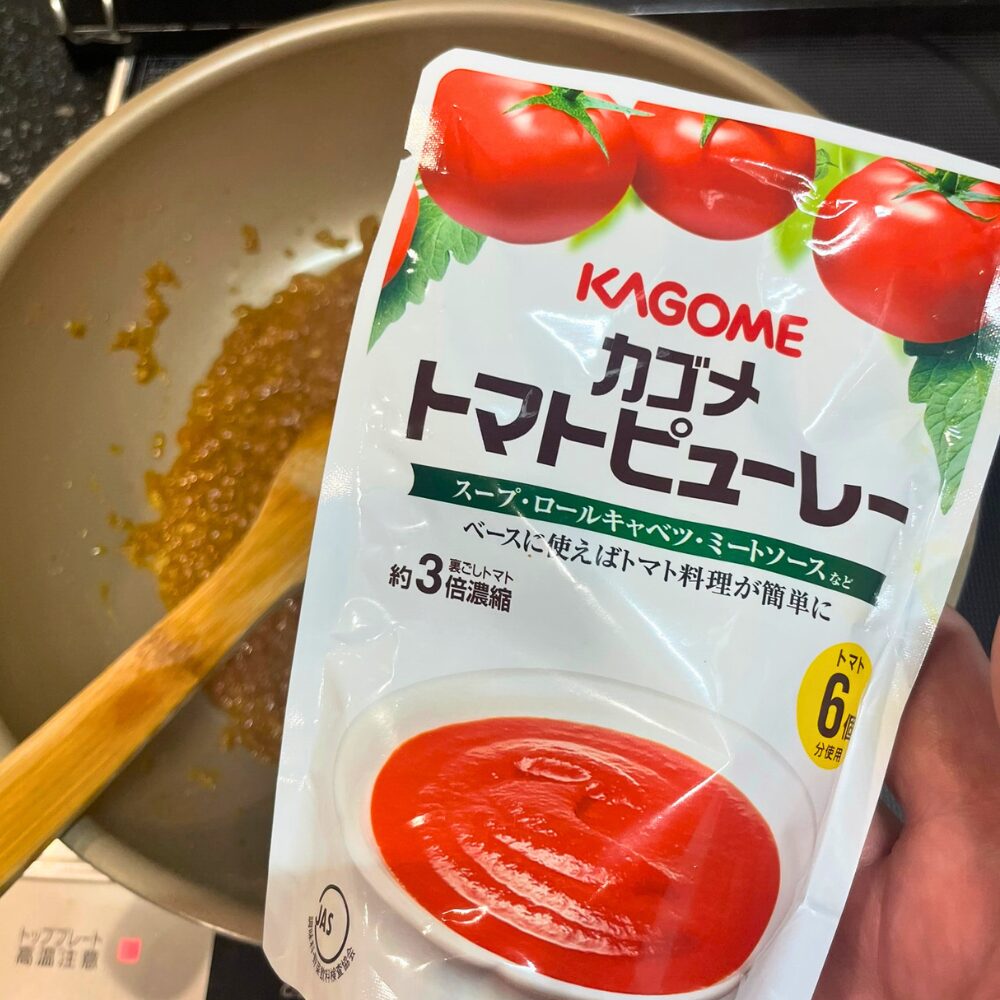 フライパンに炒めたソフリットへ、カゴメのトマトピューレと海老出汁を加える工程。トマトの酸味と海老の旨味を合わせ、中火で10分煮込むことでビスク特有の濃厚な味わいが生まれる。