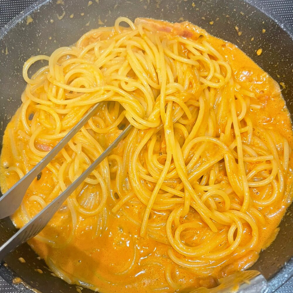 フライパンの中でビスク風ソースとスパゲッティを絡めている様子。濃厚な海老の旨味がパスタ全体にまとわりつき、つややかに仕上がっている。
