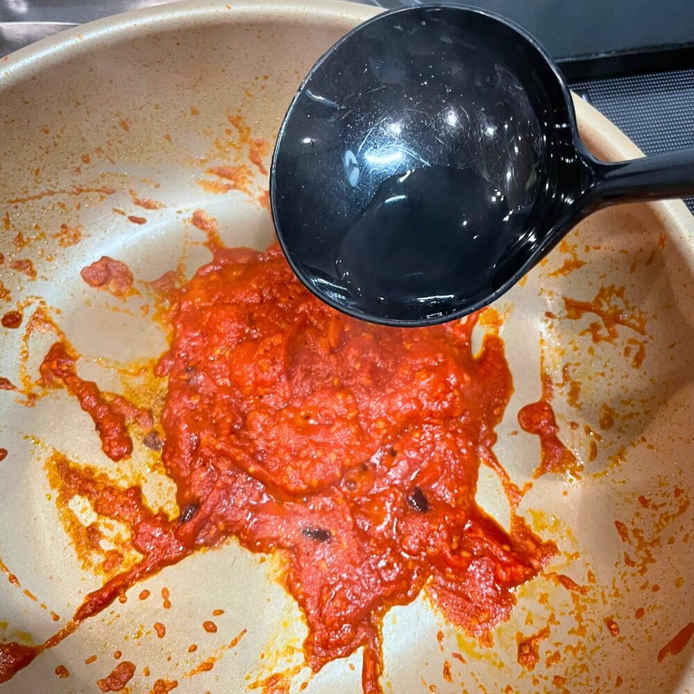 しっかり煮詰めたトマトソースに、ゆで汁をお玉で加えて濃度と塩味を調整している工程