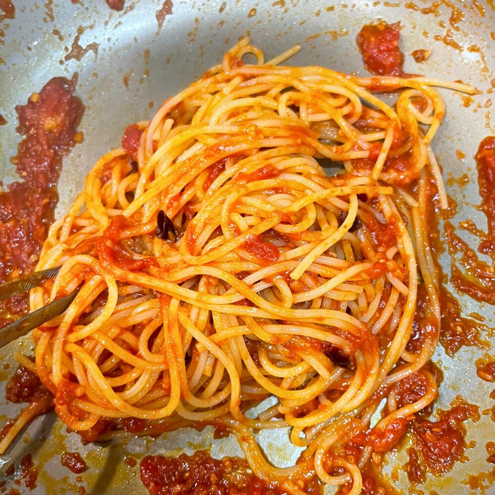 茹で上がったスパゲッティを強火のフライパンに加え、濃厚なトマトソースと素早く絡めている工程