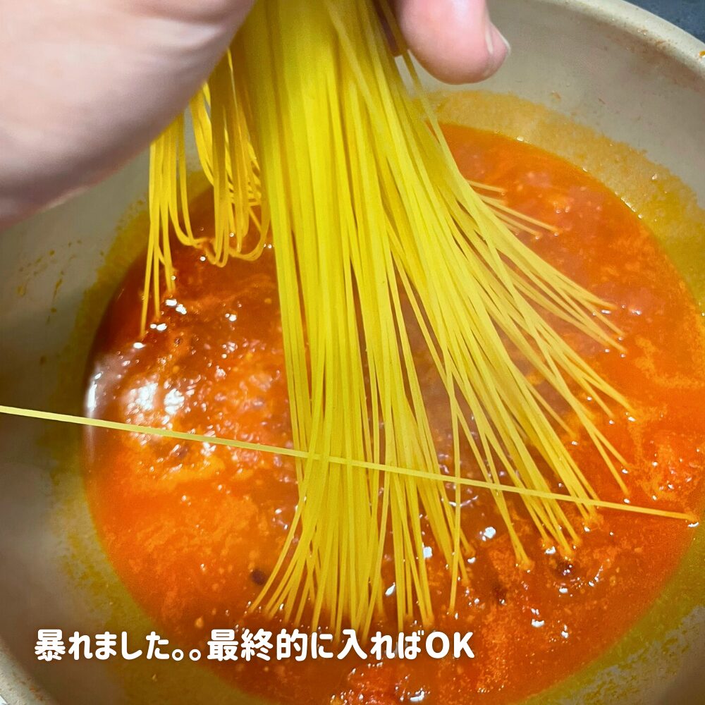 煮詰めたトマトソースに水を加えて沸騰させ、スパゲッティを折らずにそのままフライパンへ押し込んでいる様子