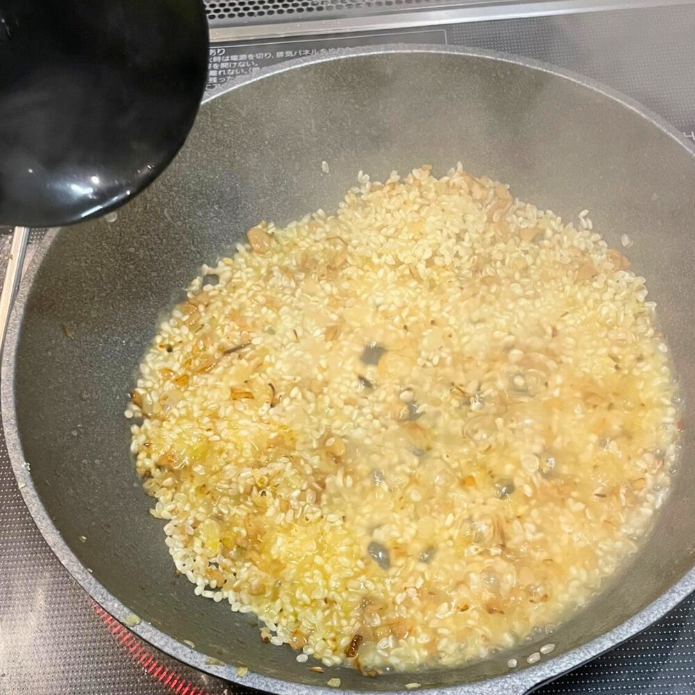 リゾットを煮込んでいる工程。お玉でスープを少しずつ加えながら、弱火で20分ほど煮込み、米が旨味を吸収している様子。