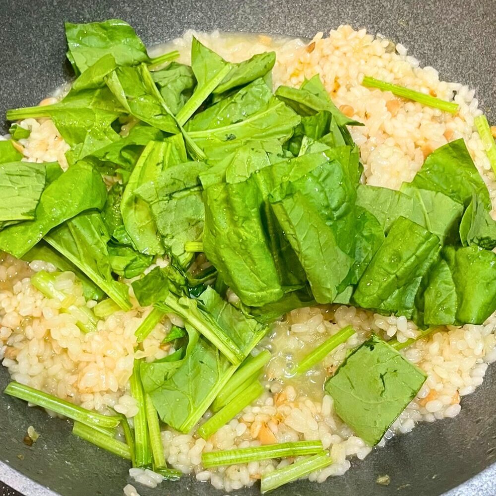 リゾットの仕上げ工程。煮込みの最後にほうれん草などの青菜を加え、余熱でさっと火を通して彩りと栄養をプラスしている様子。