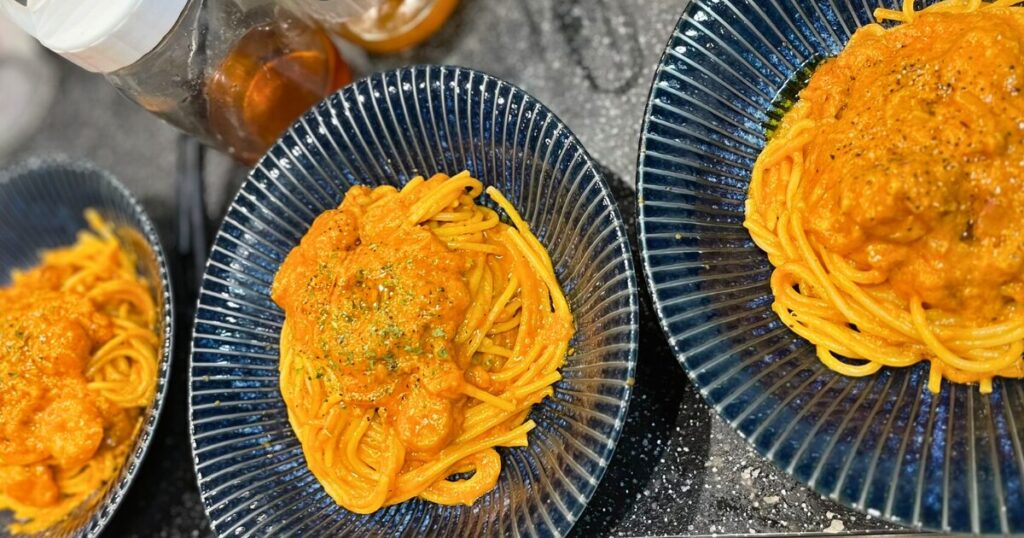 エビオイルと海老出汁で作る濃厚ビスク風パスタ。家庭でもキャンプでも手軽に再現でき、平日15分で仕上がるヒーローの一皿。青い器に盛られた鮮やかなオレンジ色のソースが特徴。